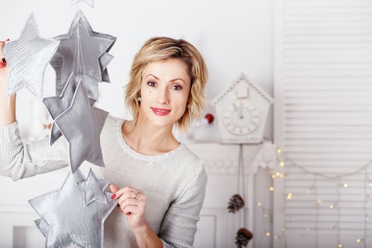 Portrait of a beautiful woman in the interior with Christmas decorations. Girl catches toy star - an element of a Christmas decor