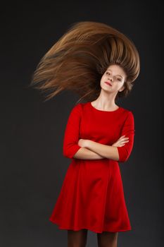 Portrait of a smiling young beautiful girl in a red dress with a flying hair. Girl with long flowing hair. Hair fluttering in motion.