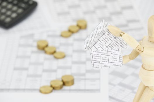 Wooden dummy holding house on finance account have blur step pile of gold coins and calculator as background.