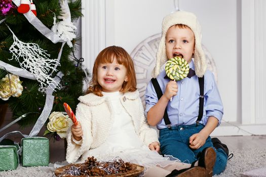Little children eating a lollipops. Portrait of two funny little kids with delicious candies in the hands. Happy children and family In anticipation of new year and Christmas.