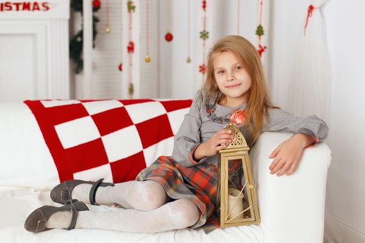 Little girl sitting on the couch and waiting for a miracle in Christmas decorations