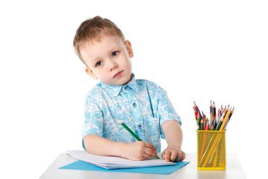 Thoughtful little boy draws with crayons isolated on white background