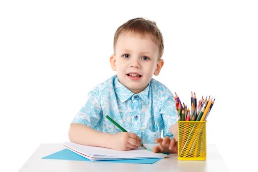 Smiling little boy draws with crayons isolated on white background
