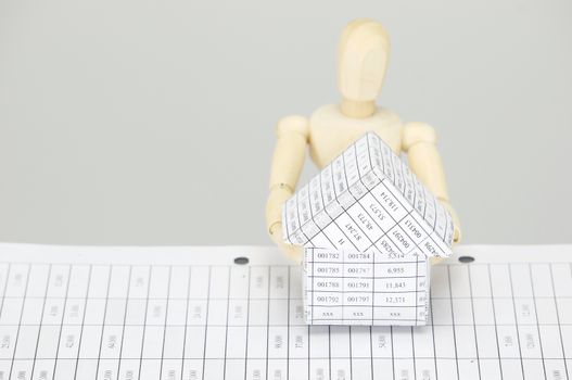 Wooden dummy holding house on finance account with white background.