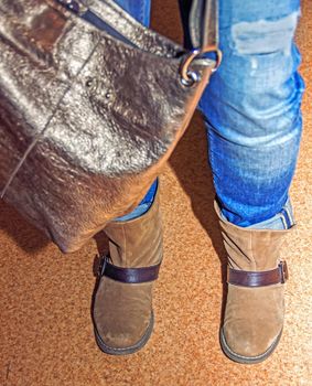 female legs in brown boots, women's shoes, bag, soft focus
