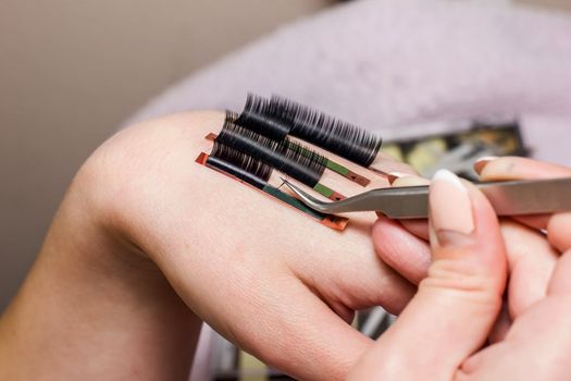 artificial eyelash extensions, the master's hand, eyelash extension procedure in a beauty salon, the beauty industry is gushing into the hands of the masters