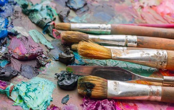 Used brushes on an artist's palette of colorful oil paint for drawing and painting