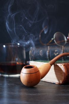 Wooden smoking pipe on old book near glass of alcohol