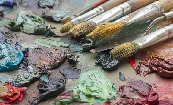 used brushes in an artist's palette of colorful oil paint for drawing and painting