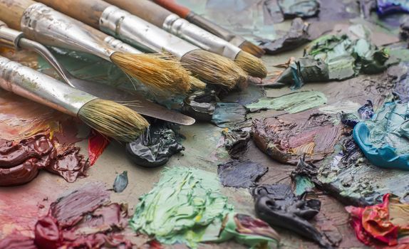 used brushes in an artist's palette of colorful oil paint for drawing and painting