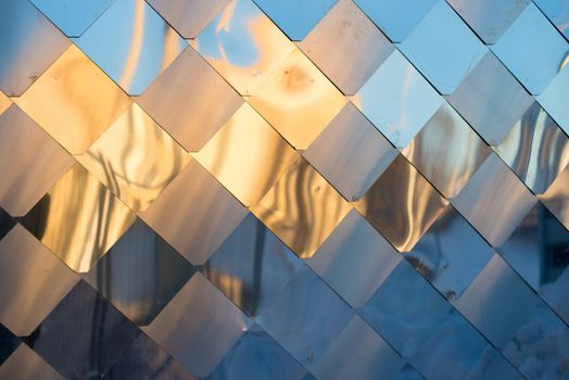 old, dirty aluminum metal wall facade panel with rhombus, similar to the scales and tiles. Reflection of sunset