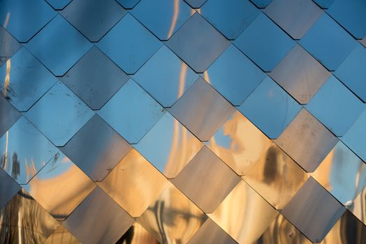 old, dirty aluminum metal wall facade panel with rhombus, similar to the scales and tiles. Reflection of sunset
