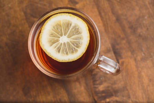 Top view of black tea with lemon on wooden plank table.