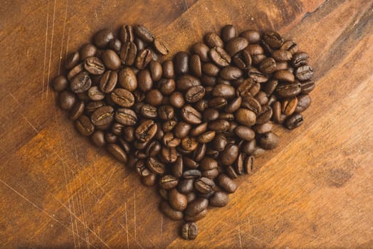 Brown coffee beans in  shape of heart, closeup of macro coffee beans for background and texture. On brown wooden board