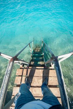 Old vintage metal wooden stairs leading to blue turquoise sea water from beach. Beautiful summer day. Swimming pool with grunge retro stairs on the ocean coast. Top POV, Point of view shot.