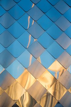 old, dirty aluminum metal wall facade panel with rhombus, similar to the scales and tiles. Reflection of sunset