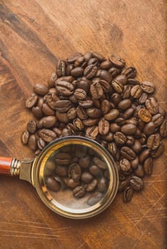 Brown coffee beans in circle shape, closeup of macro coffee beans for background and texture. On brown wooden board with magnify glass. Copyspace.