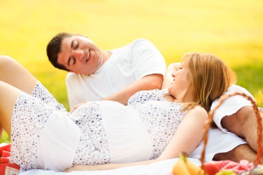 husband and pregnant wife relaxing on summer day in the park