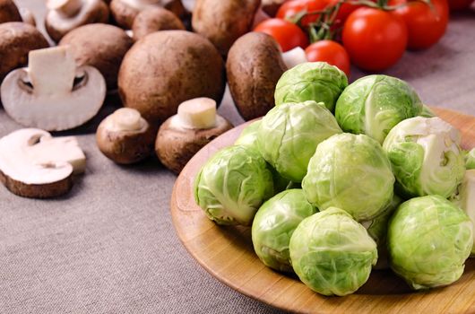 Several heads of fresh wet brussels sprouts on a wooden plate, cherry tomatoes on a linen fabric .