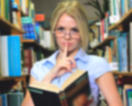 Young girl student, a teacher reading a book in the library among the bookshelves, silence, quiet demeanor blurred