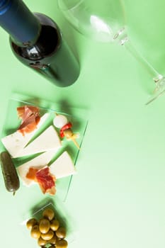 Top view of a bottle of red wine, a glass, olives, cheese and ham