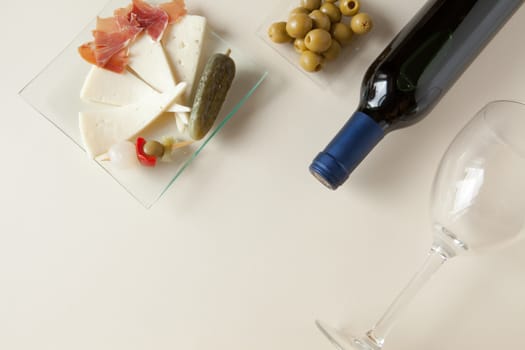 Top view of a bottle of red wine, a glass, olives, cheese and ham
