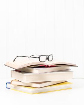 Small stack of hardcover books with eyeglasses sitting on top.