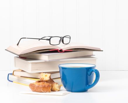 Fresh coffee and a donut in front of a small stack of textbooks.