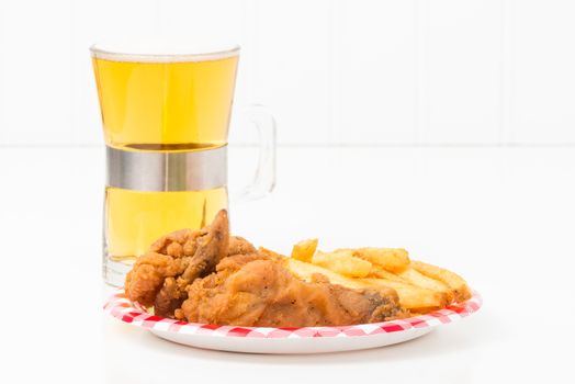 Small paper plate with pieces of southern fried chicken and french fried potatoes.