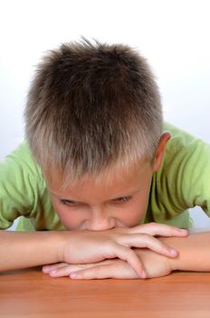 Serious school boy sitting thinking at the table