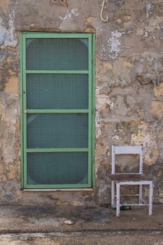 One of the weekend houses in a fishing village at the island Malta. Old stone walls, green door. Old white empty chair.