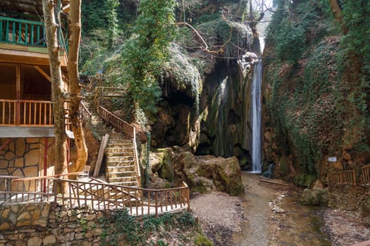 View of a small waterfall flowing around big rocks with small plants and wooden stairs.