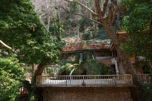 View of a small waterfall flowing around big rocks with small plants and wooden stairs.