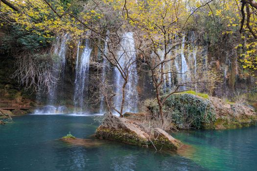 View of Kursunlu Waterfall in Antalya, flowing from high, with green trees and plants around.