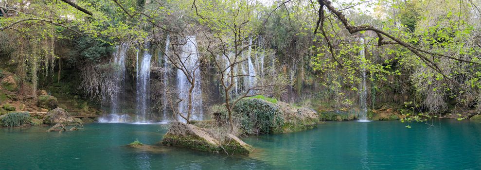 View of Kursunlu Waterfall in Antalya, flowing from high, with green trees and plants around.