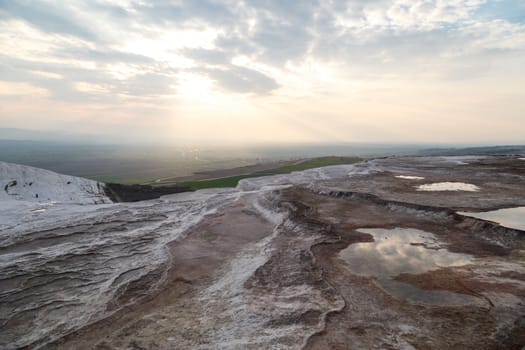 General view of Pamukkale Travertines with geographical formations on cloudy sky background at sunset time.