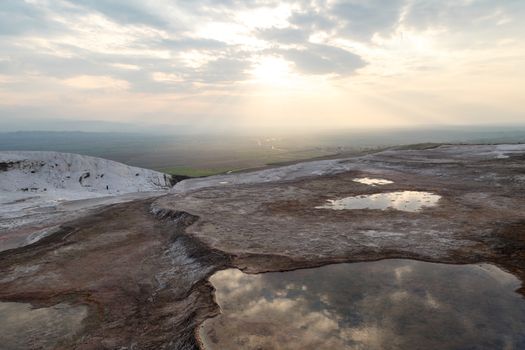 General view of Pamukkale Travertines with geographical formations on cloudy sky background at sunset time.