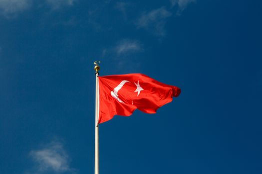 View of red and white Turkish flag with a moon and star on bright blue sky background.