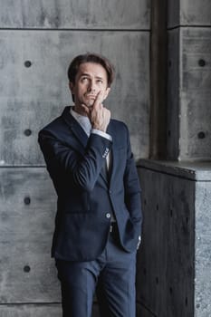 Portrait of a pensive businessman in suit over concrete wall background