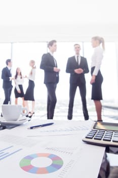 Close-up of financial reports and calculator, business people team standing in the background