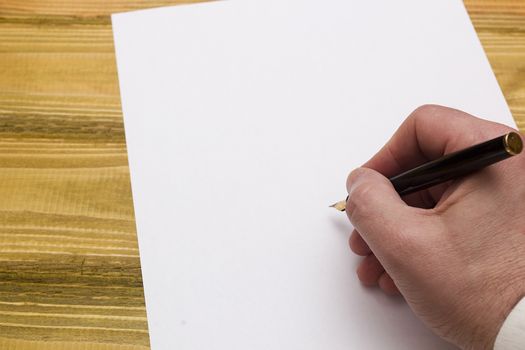 Hand with pen writing on a blank paper on a wooden table