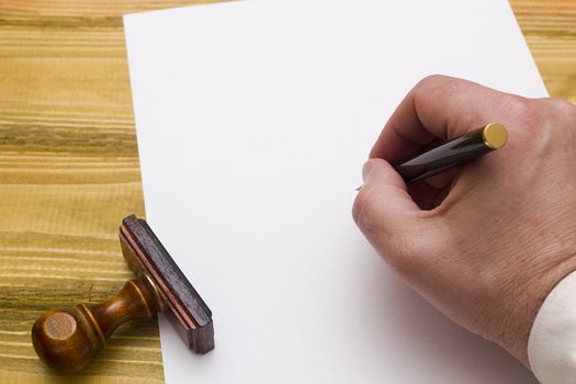 Hand with pen writing on a blank paper on a wooden table