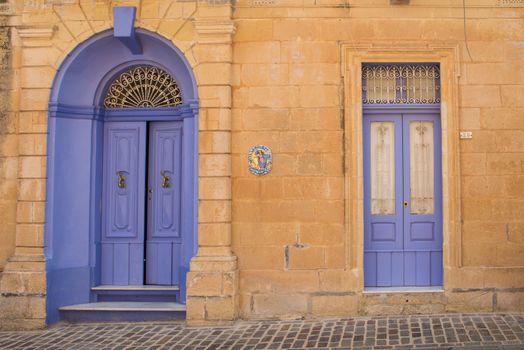 Well preserved house made of stones with small and big doors painted unusual violet color. Small city Had-Dingli at the mediterranean island Malta.