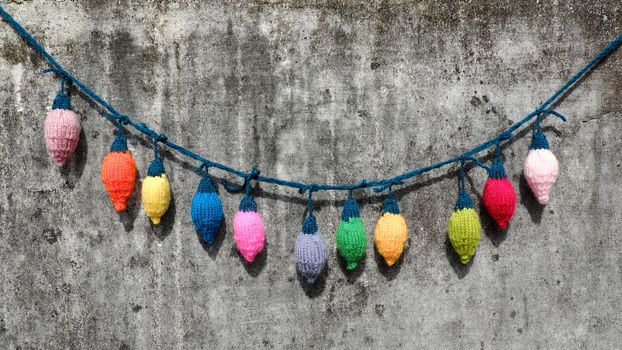 Group of colorful Xmas ornament for winter holiday, handmade product, knitted Christmas lights bulb on old wall background