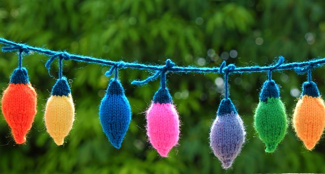 Group of colorful Xmas ornament for winter holiday, handmade product, knitted Christmas lights bulb on green background