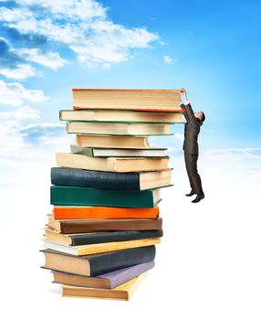 Businessman hanging on top of stack books blue sky background.