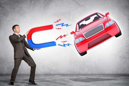 Businessman in suit holding big magnet attracting car