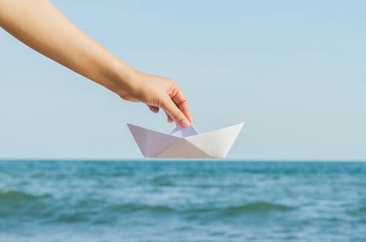 Female hand holding paper boat on the sea background