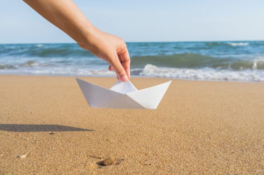 Female hand holding paper boat on the sea background
