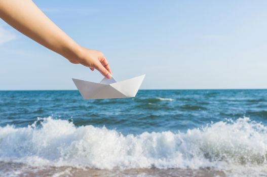 Female hand holding paper boat on the sea background